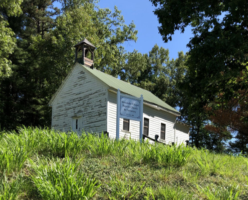 Photo of white one-room structure on hill with sign in front