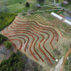 Aerial view of farm with fresh contour line trench dug on hillside below greenhouses.