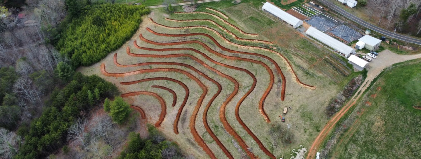 Aerial view of farm with fresh contour line trench dug on hillside below greenhouses.
