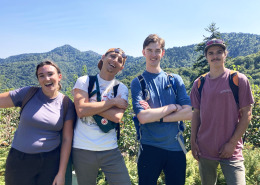 Group of four young adults smiling, some with arms crossed, with mountain ridgeline in background