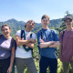 Group of four young adults smiling, some with arms crossed, with mountain ridgeline in background