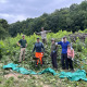 A group of volunteers stands with cut brush surrounded by pasture and forest.