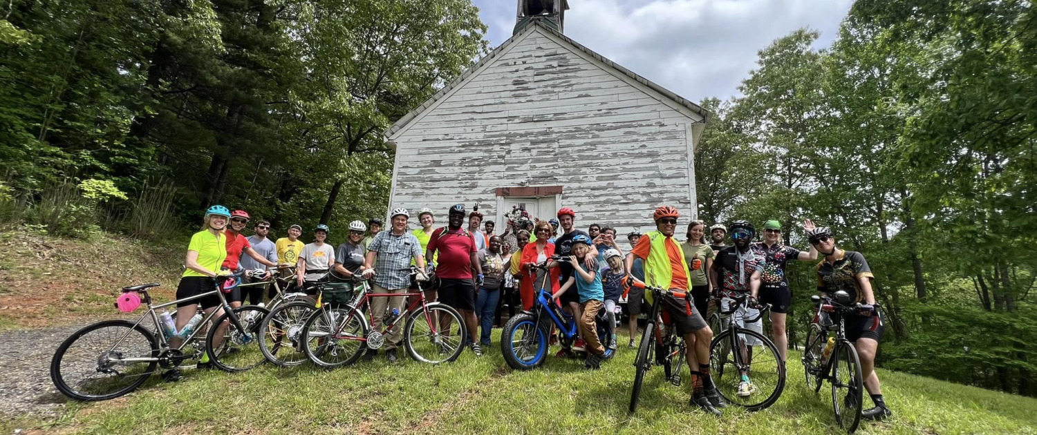 group of cyclists gathered in front of historic white church building