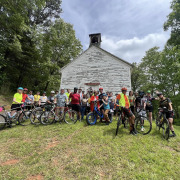 group of cyclists gathered in front of historic white church building