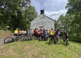 group of cyclists gathered in front of historic white church building