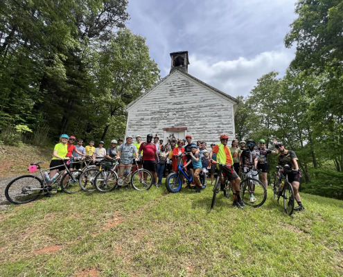 group of cyclists gathered in front of historic white church building