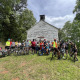 group of cyclists gathered in front of historic white church building